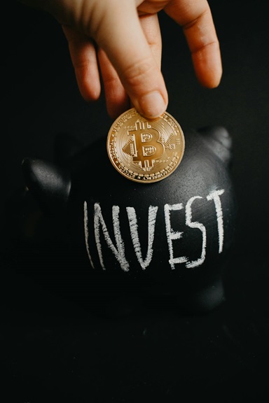 Fingers holding bitcoin over the word INVEST