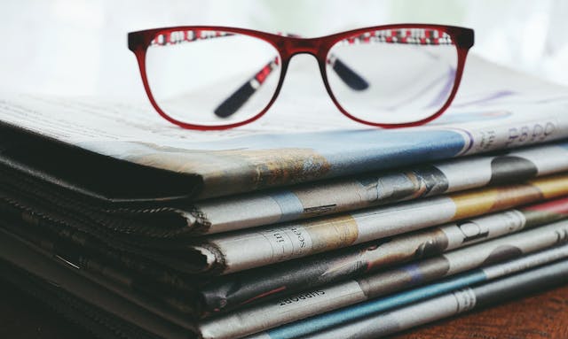 eyeglasses on top of stack of newspapers